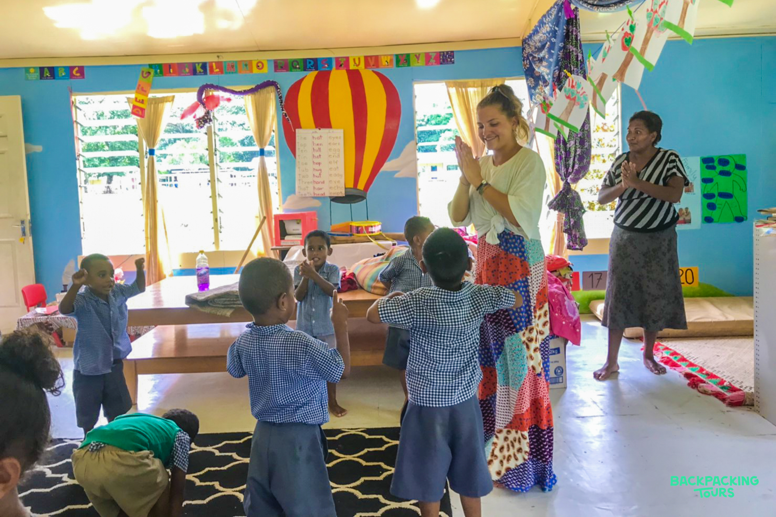 Children and teachers happily engage in a group activity inside a colorful kindergarten classroom in Fiji.