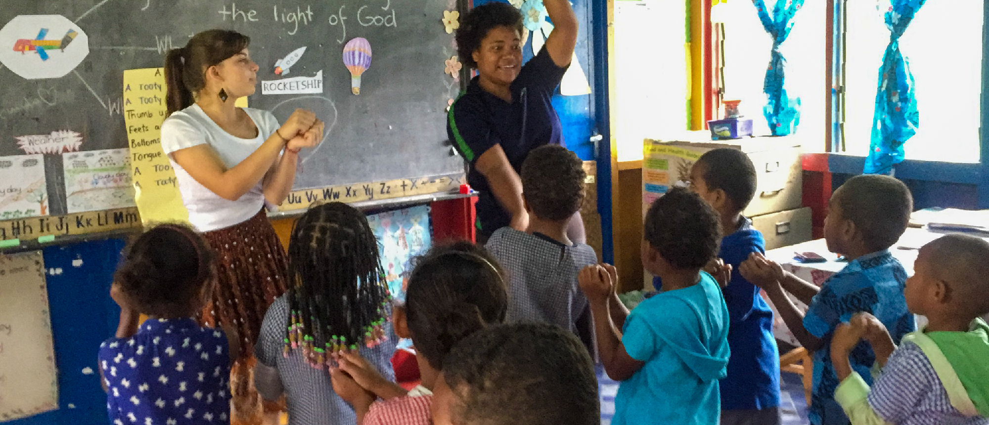 Two volunteers teach young children in a colorful classroom, leading an interactive activity.