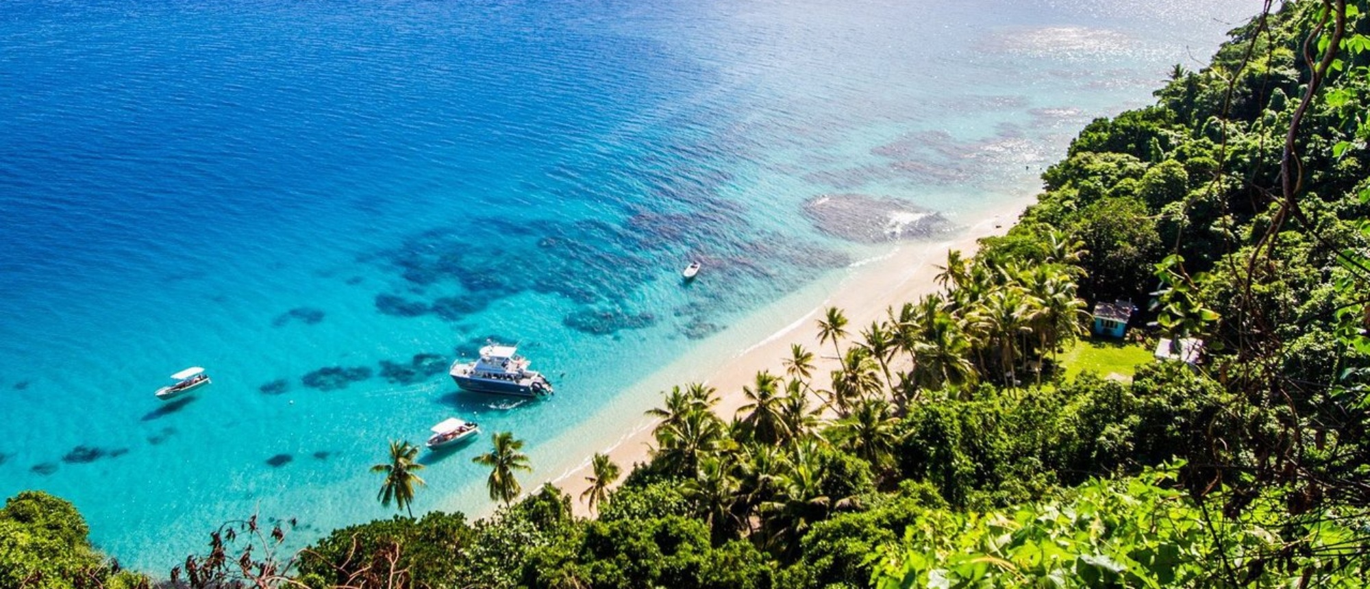 Stunning aerial view of Yanuca Island's tropical beach with boats on clear water and lush trees.
