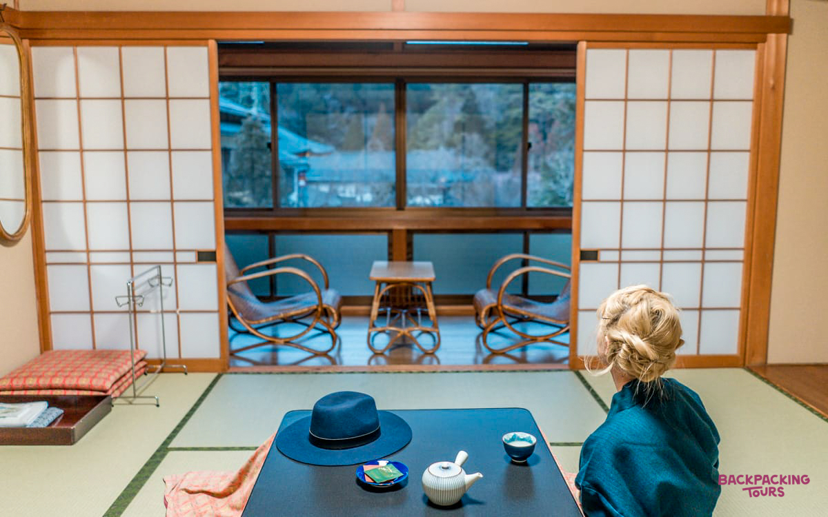 A traveler relaxes in a serene Koyasan temple room, admiring the peaceful mountain view.