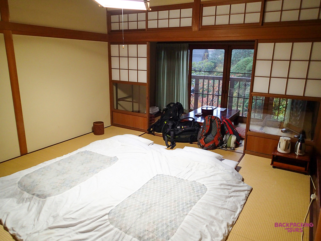 A serene Koyasan temple room with futons, tatami mats, and a view of lush mountain greenery.