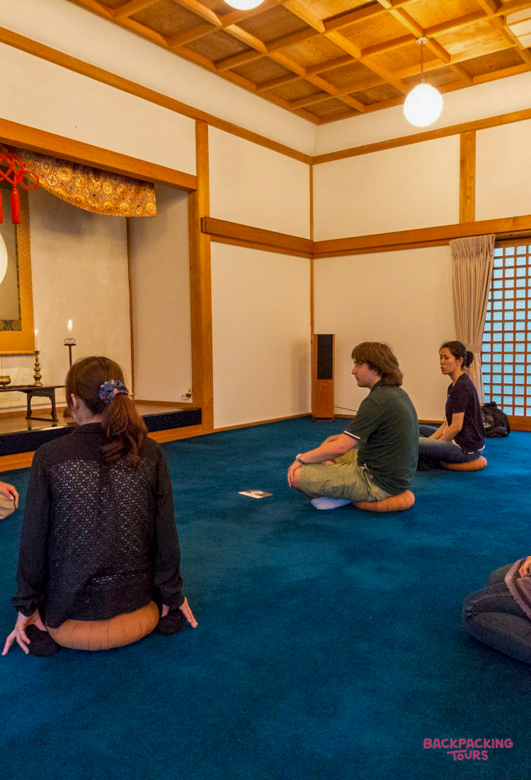 Travelers sit on cushions in a serene Japanese temple room, participating in a meditative session at Koyasan.