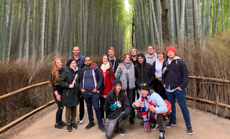 A happy group of diverse backpackers posing on a path in the dense Arashiyama bamboo forest.