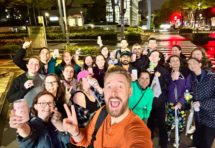 A joyful group of friends taking a selfie on a wet city street at night, holding drinks.