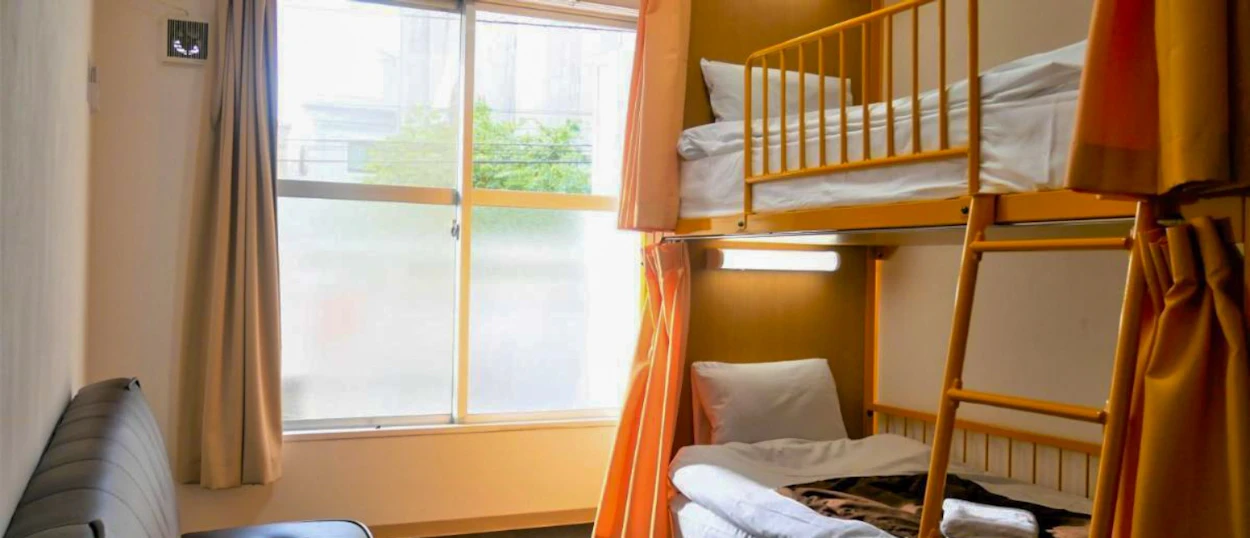 A bright and clean hostel room in Tokyo with a wooden bunk bed and privacy curtains.