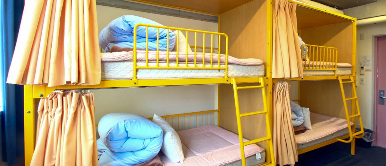 Bright yellow bunk beds with privacy curtains in a clean Tokyo hostel dorm room.
