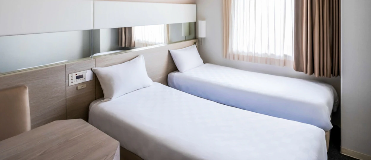 A clean, modern hotel room with two single beds, white bedding, and a small table in Osaka.