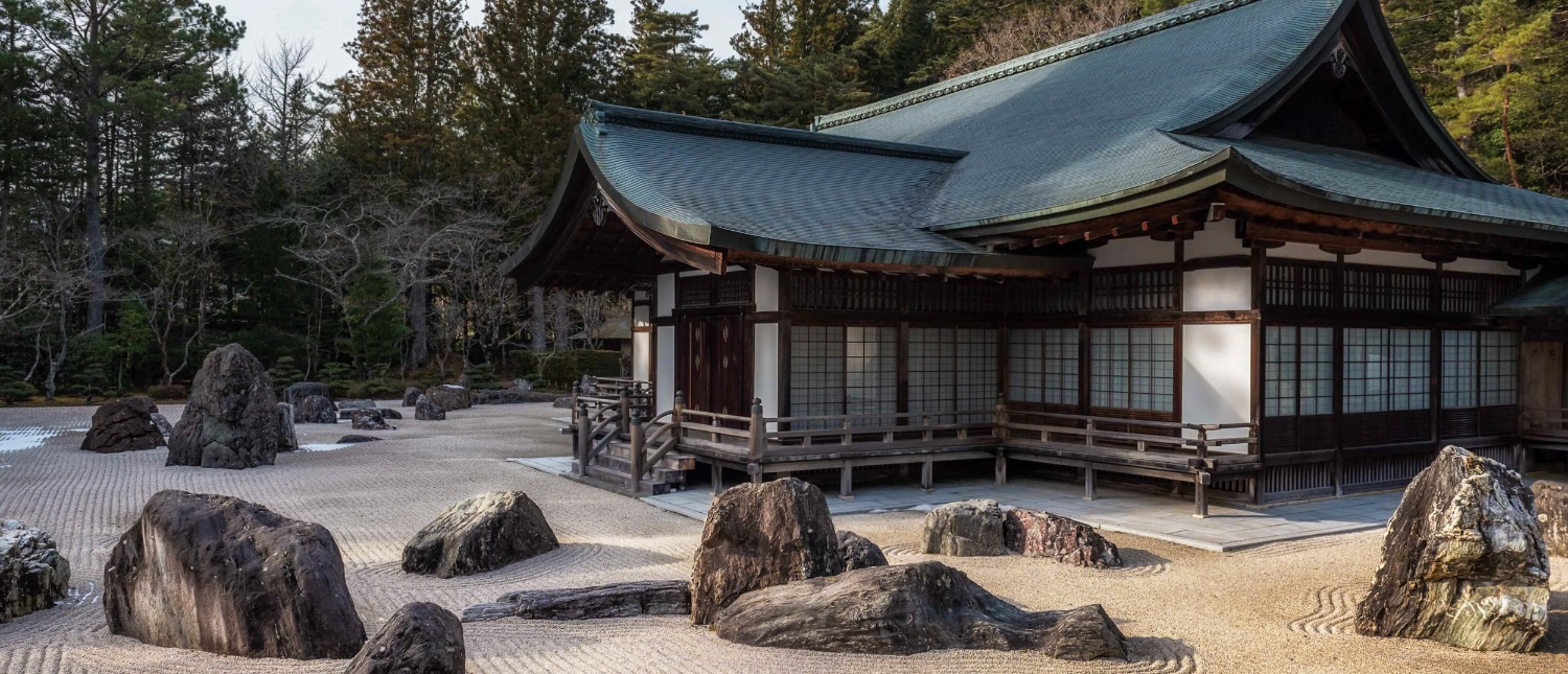 A traditional Japanese temple overlooks a tranquil rock garden with raked sand and large stones in Koyasan.