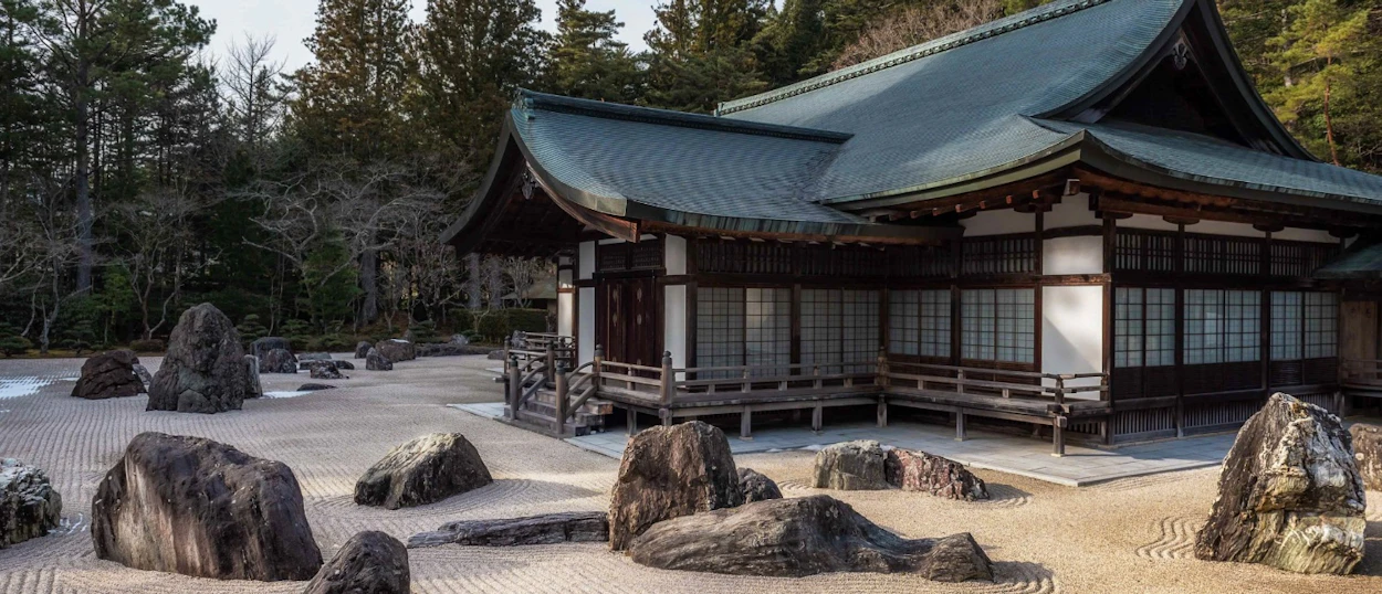 A traditional Japanese temple overlooks a tranquil rock garden with raked sand and large stones in Koyasan.