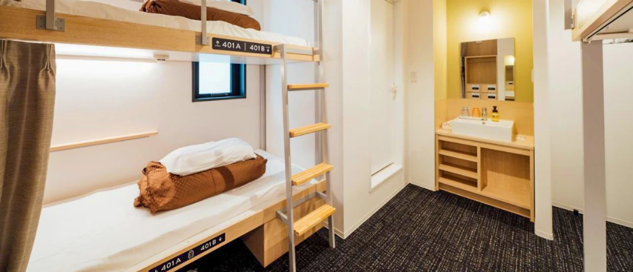 A clean, modern hostel room in Hiroshima with bunk beds, a ladder, and a small sink area.