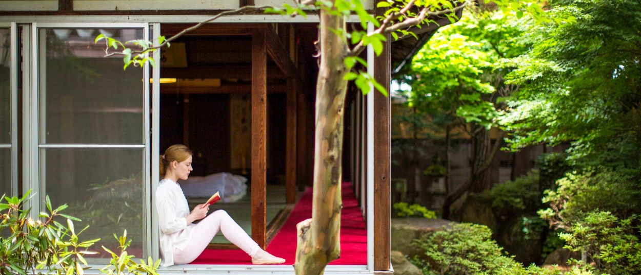 A woman peacefully reads a book at a Japanese temple with a serene garden view in Takayama.