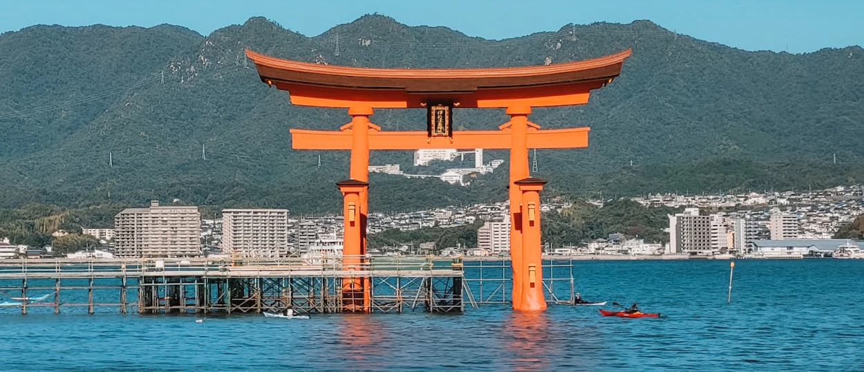 The iconic orange torii gate of Miyajima Island stands in the sea, surrounded by structures.