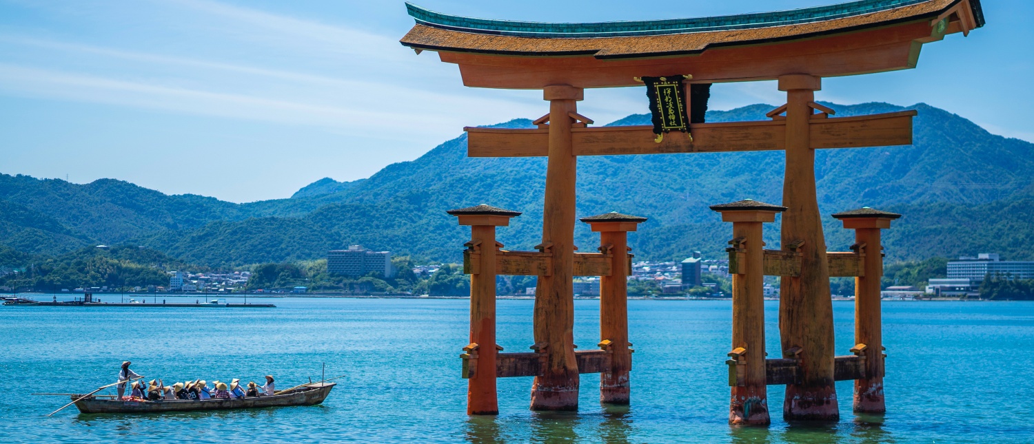 The iconic Great Torii Gate of Miyajima Island stands in the sea, with a boat passing by.