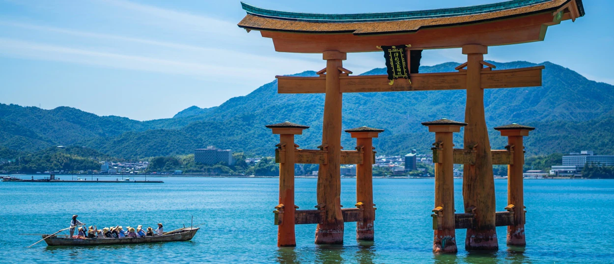 The iconic Great Torii Gate of Miyajima Island stands in the sea, with a boat passing by.