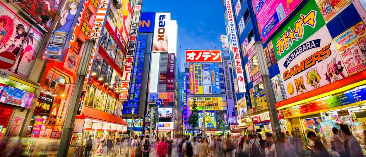 A vibrant street scene in Tokyo's Akihabara district, bustling with people and colorful neon signs.