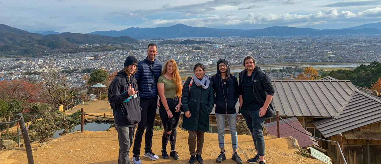 Six happy backpackers pose on a mountain overlooking the sprawling city of Hakone, Japan.