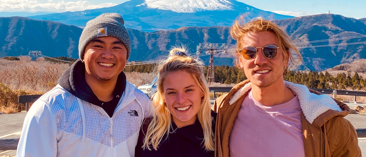 Three happy backpackers smiling with snow-capped Mount Fuji and mountains in Hakone, Japan.