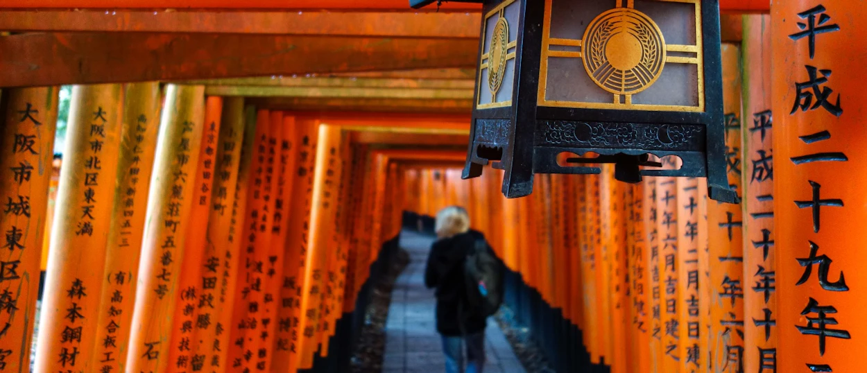 A person explores the iconic bright orange torii gates of Fushimi Inari Shrine in Kyoto.