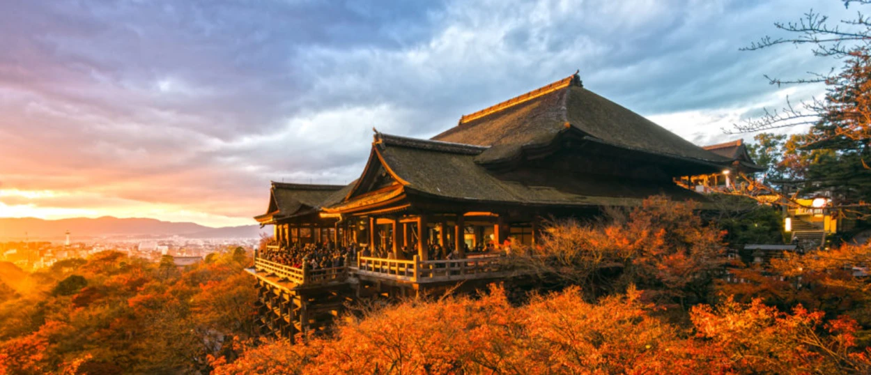 Kiyomizu-dera Temple in Kyoto, bathed in warm sunset light, surrounded by vibrant autumn foliage.