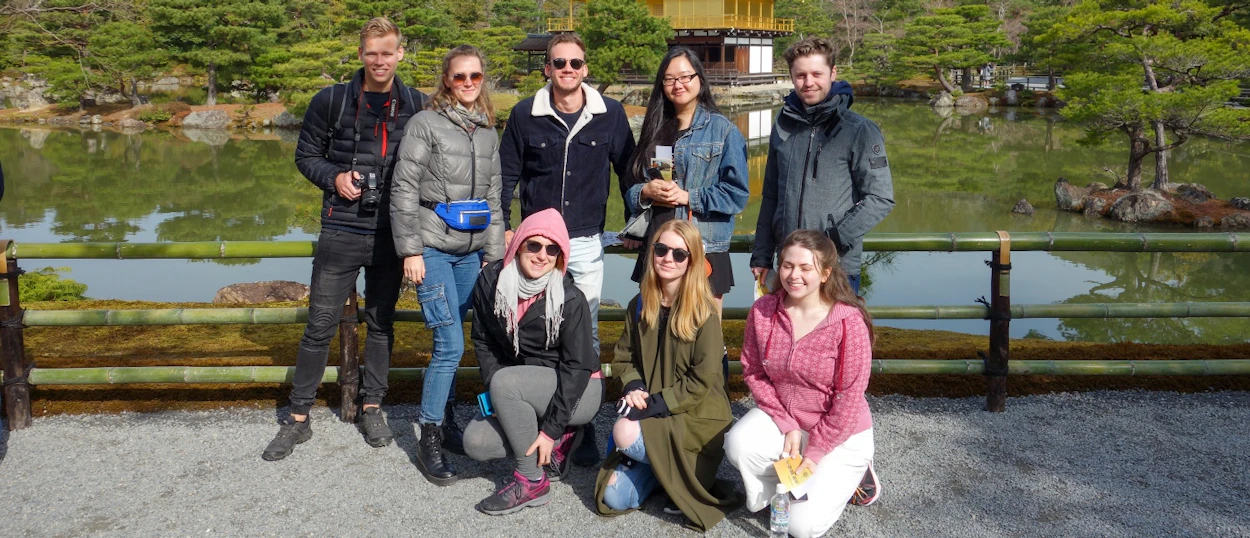 A group of eight happy travelers pose in front of Kyoto's Golden Pavilion and its tranquil pond.