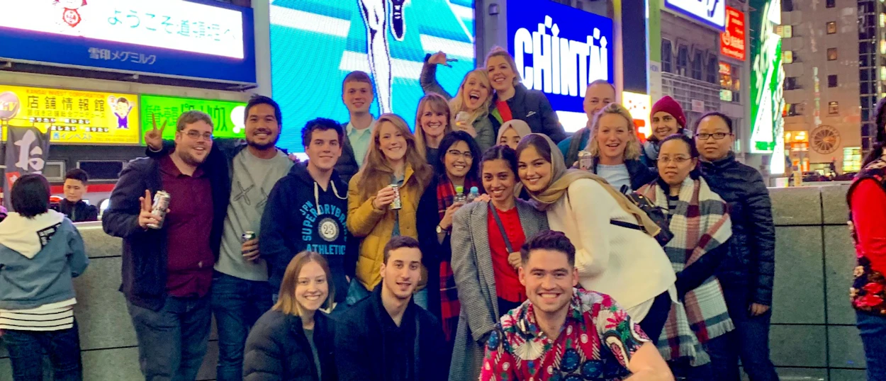 Happy young travelers pose for a group photo at night amidst bright neon signs in Osaka.