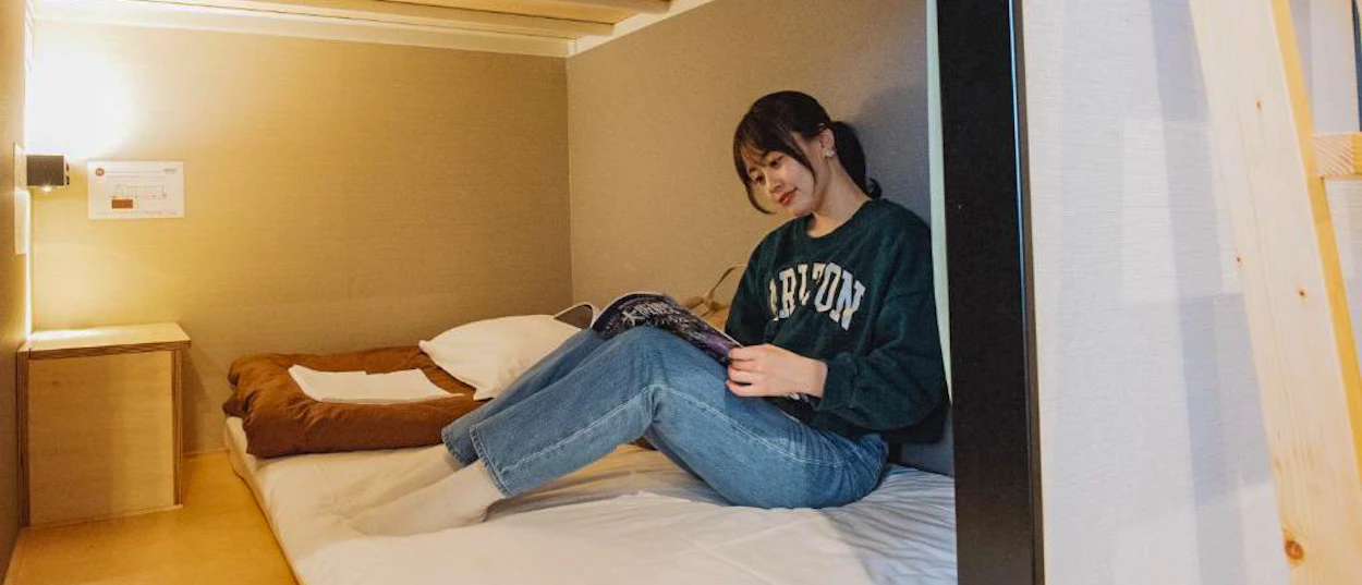 Smiling woman relaxing on a hostel bunk bed, reading a book in Osaka.