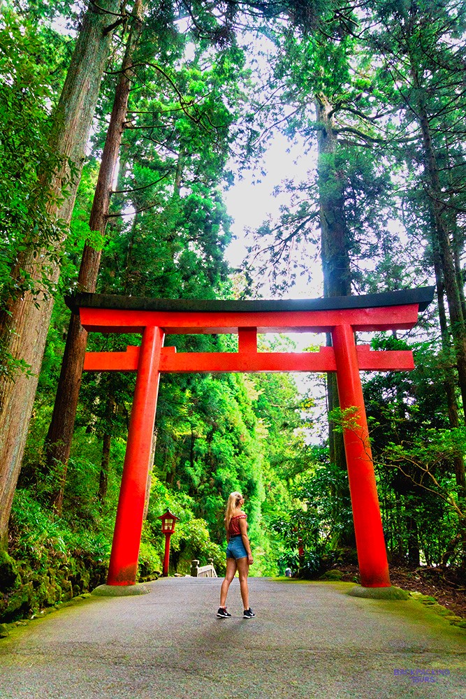 Traveller running beneath a giant red torii gate on a forest path in Hakone