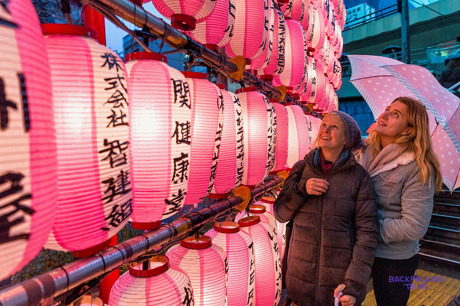 Travellers beside a wall of glowing pink lanterns in Tokyo