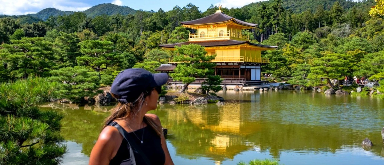 Traveller admiring the Golden Pavilion reflected in its lake in Kyoto