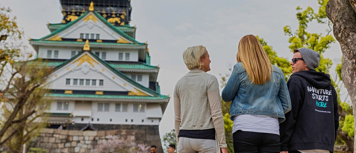 Travellers looking up at Osaka Castle and its surrounding gardens