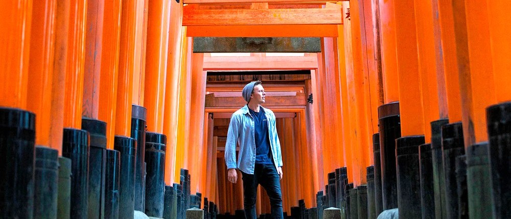 Traveller walking through the endless vermilion torii gates of Fushimi-Inari