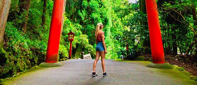 Traveller running beneath a giant red torii gate on a forest path in Hakone
