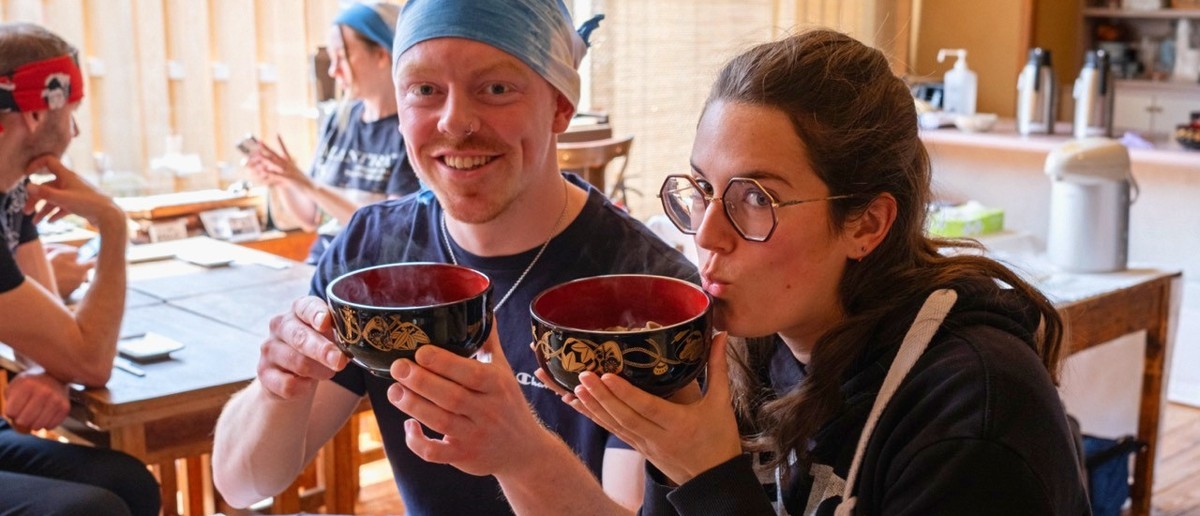 Two travellers tasting the soba noodles they made themselves