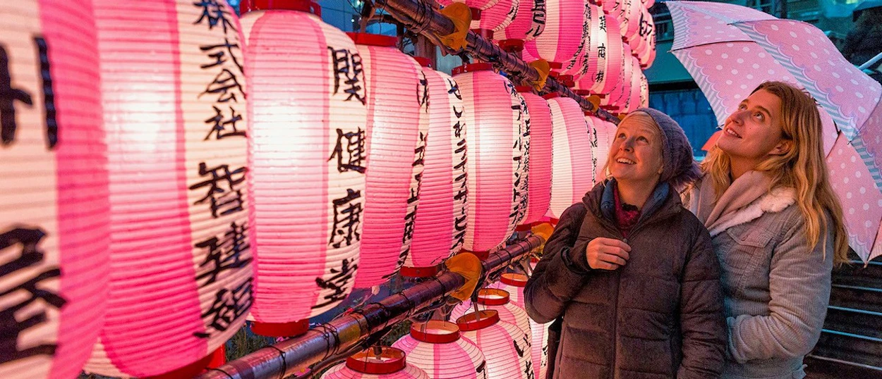 Travellers beside a wall of glowing pink lanterns in Tokyo