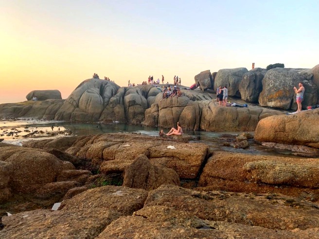 People sitting and climbing on huge granite boulders along the shore at sunset