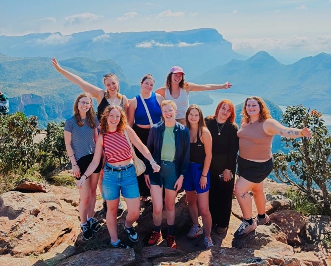 Group of travellers celebrating on a rocky viewpoint above a deep, forested canyon