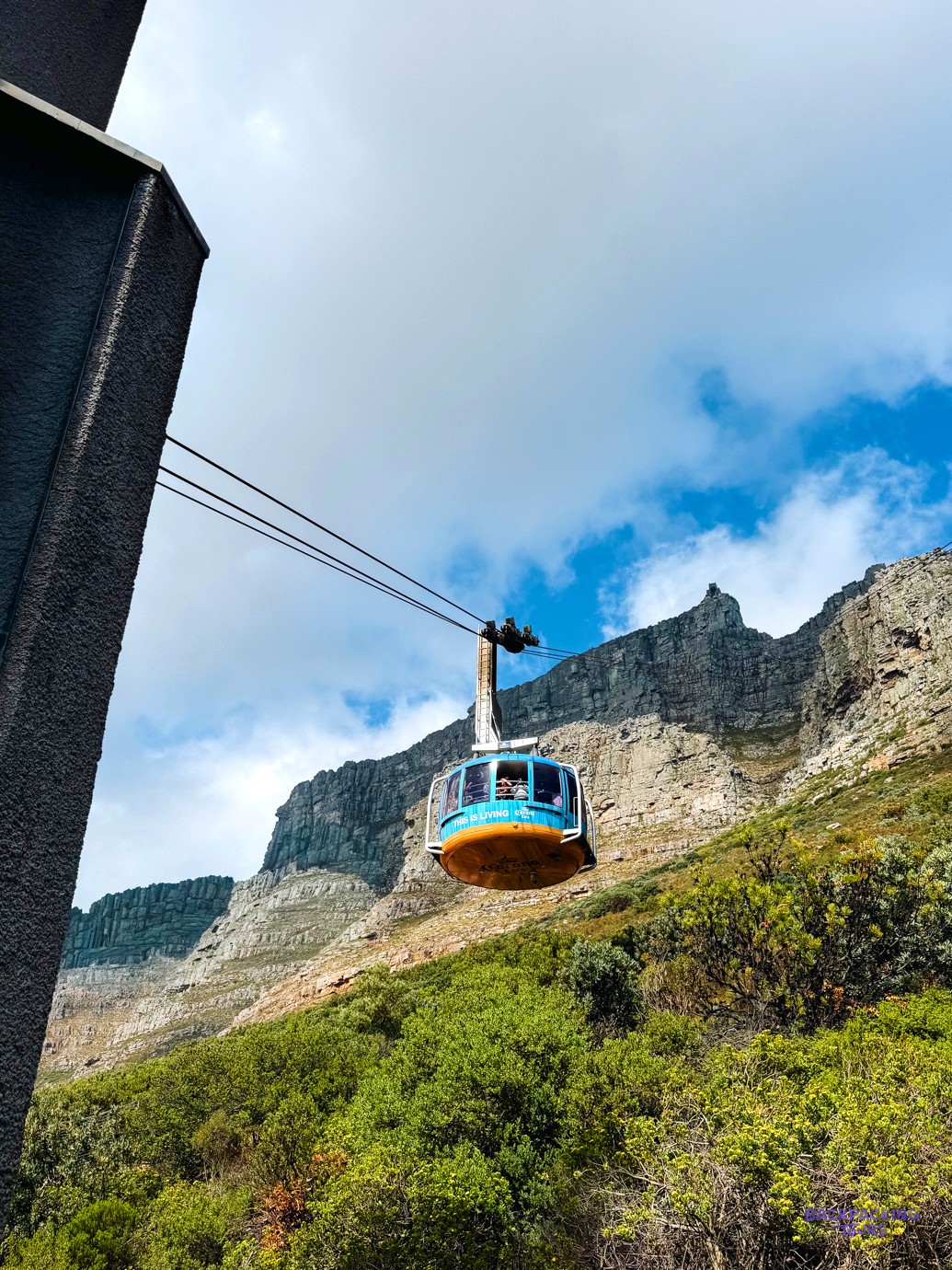 Table Mountain cable car gliding up past sheer cliffs against a bright blue sky