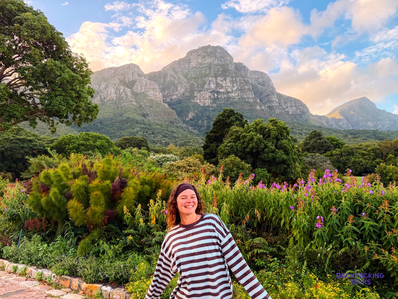 Smiling traveller in a flowering botanical garden below dramatic mountain cliffs