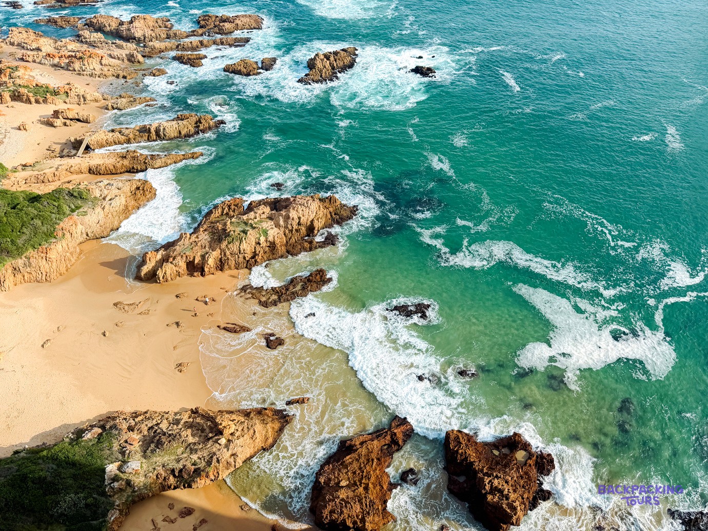 Aerial view of turquoise waves breaking over rocky outcrops and a sandy cove