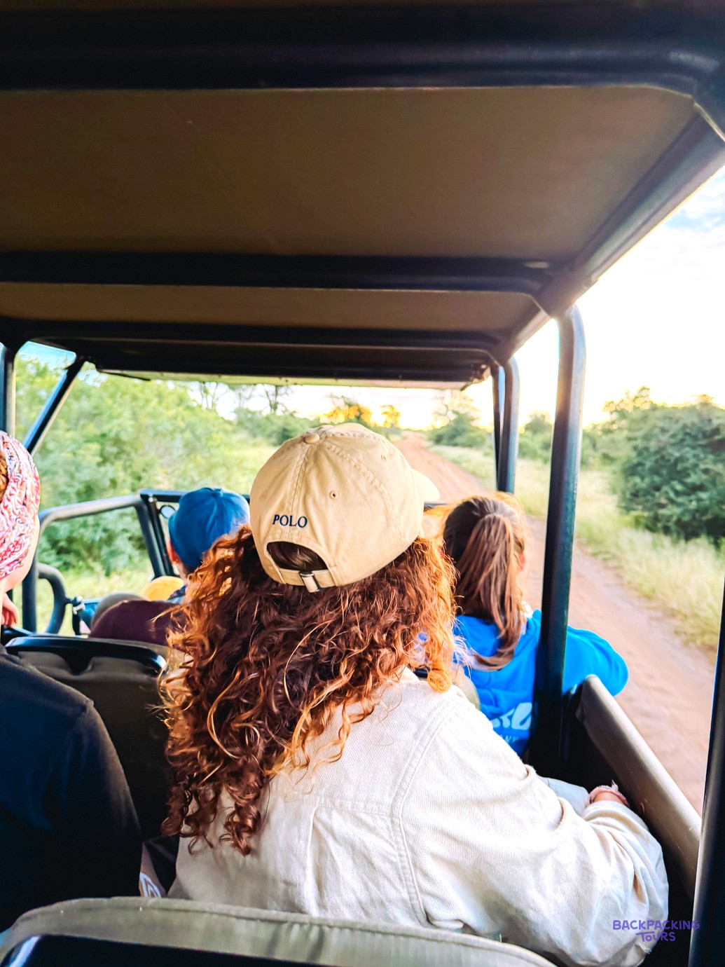 Travellers in caps looking out from the seats of an open safari vehicle on a game drive