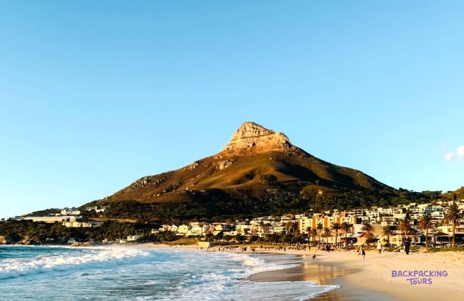 Lion's Head rising above a seaside suburb and surf rolling onto a sandy beach