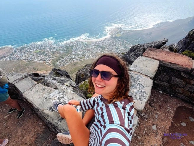 Traveller in sunglasses smiling on a clifftop ledge high above the city and coastline