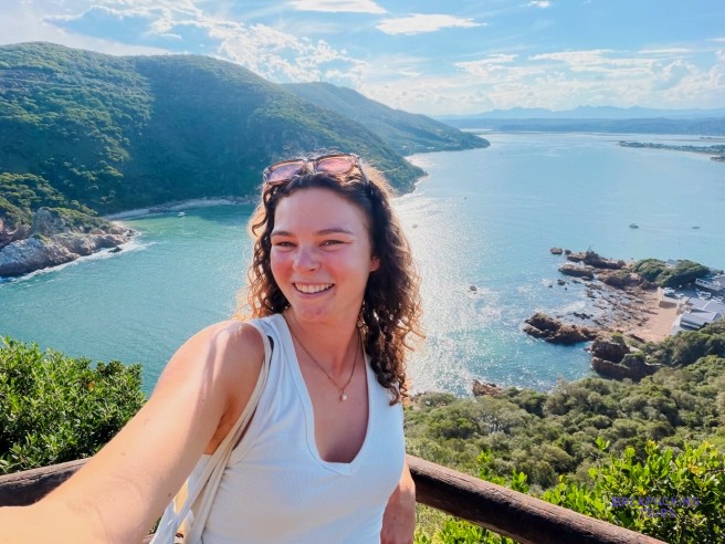 Traveller taking a selfie at a viewpoint above a calm blue inlet and rocky headland