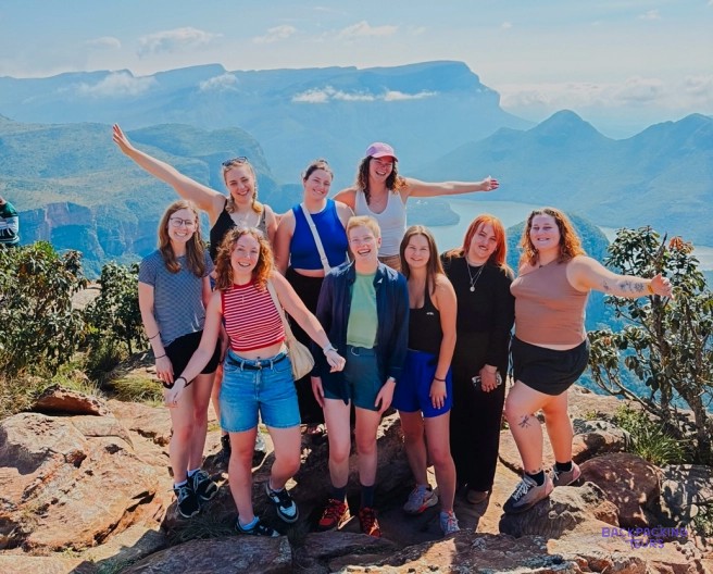 Group of travellers celebrating on a rocky viewpoint above a deep, forested canyon
