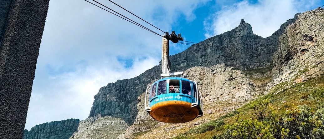 Table Mountain cable car gliding up past sheer cliffs against a bright blue sky