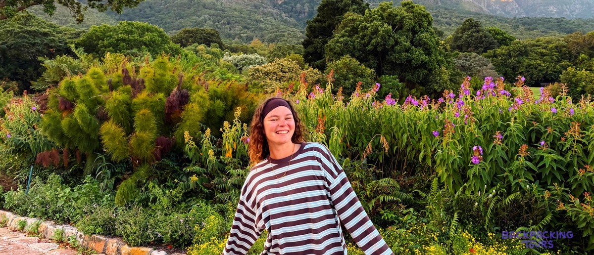 Smiling traveller in a flowering botanical garden below dramatic mountain cliffs
