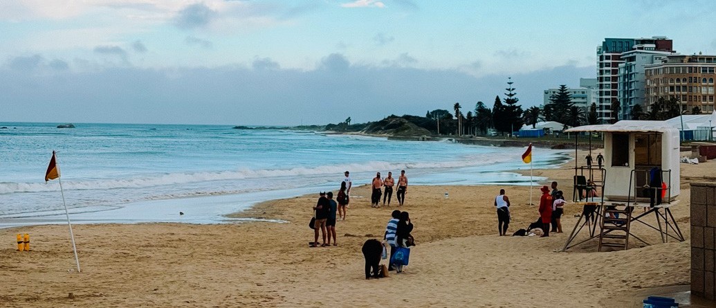 Sandy beach with a lifeguard hut, swimmers and seafront apartment blocks under a blue sky