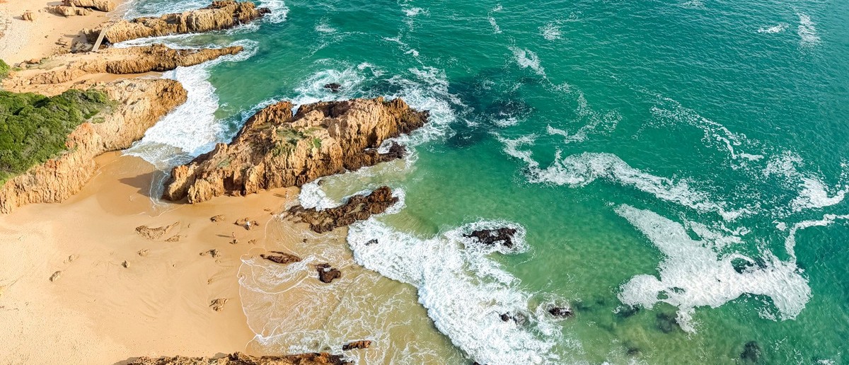 Aerial view of turquoise waves breaking over rocky outcrops and a sandy cove