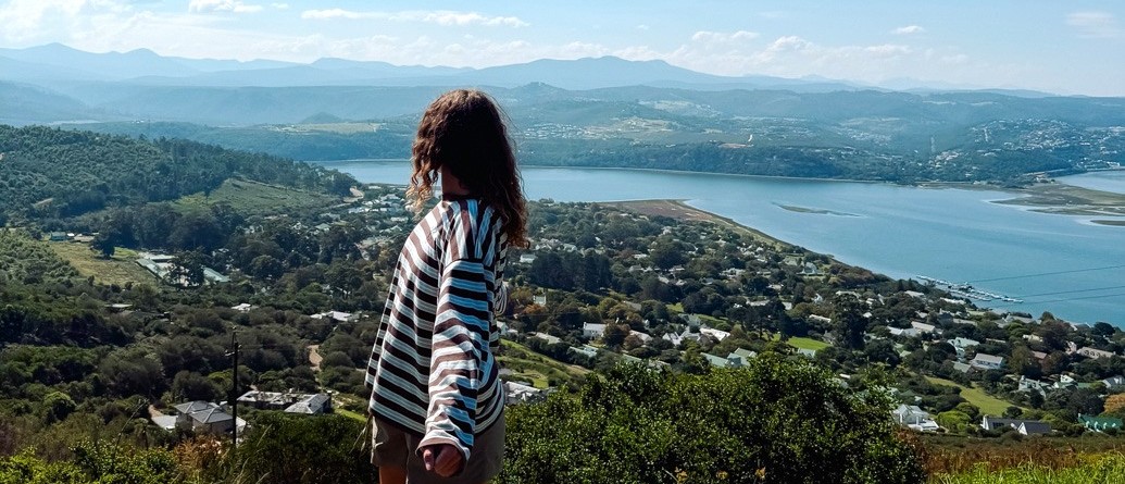 Traveller on a grassy hillside looking out over a wide lagoon and wooded town