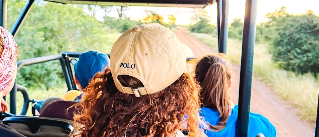 Travellers in caps looking out from the seats of an open safari vehicle on a game drive